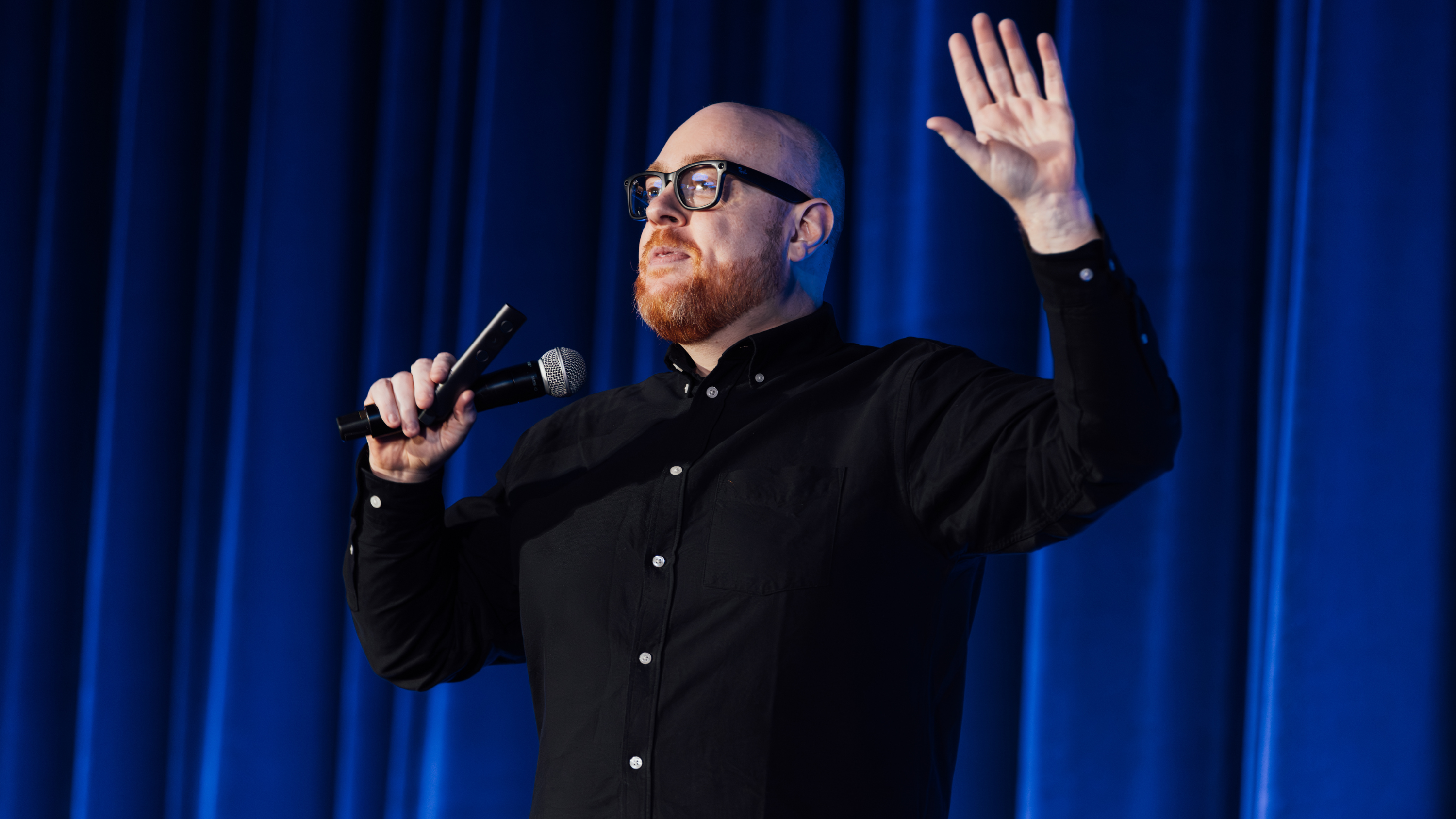 Dan Fitzpatrick speaking into a microphone beneath blue stage lights